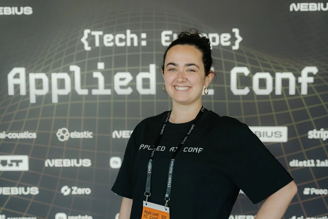 A volunteer in front of the Applied AI Conf 2026 logo wall